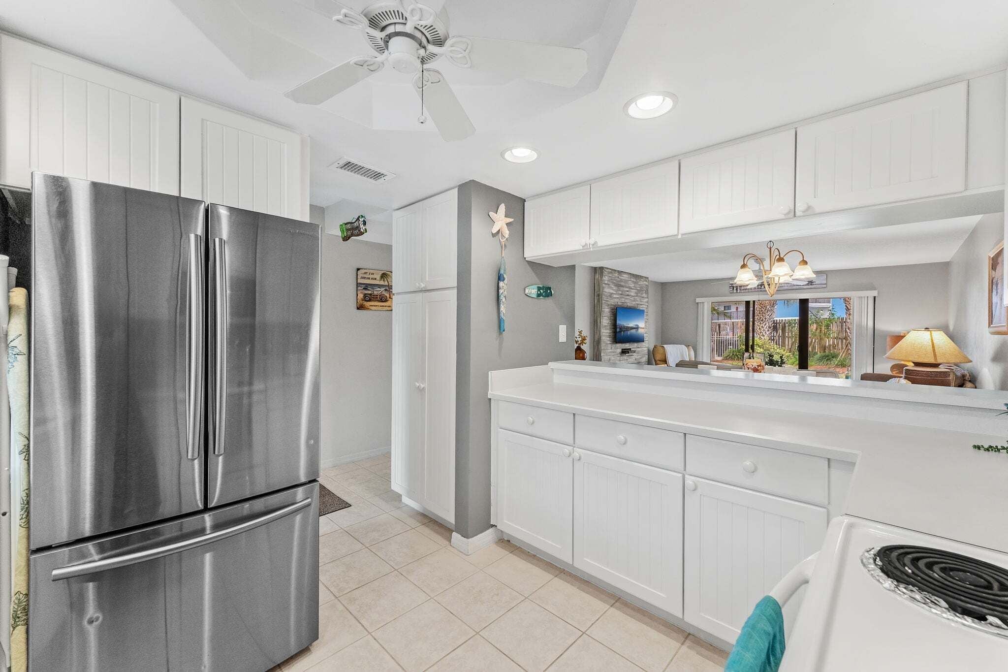 A kitchen with white cabinetry, a stainless steel refrigerator, a stove, and a ceiling fan.