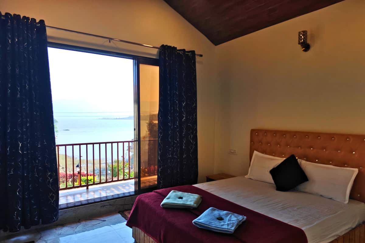 Un dormitorio con cama, vista al mar y balcón con cortinas.