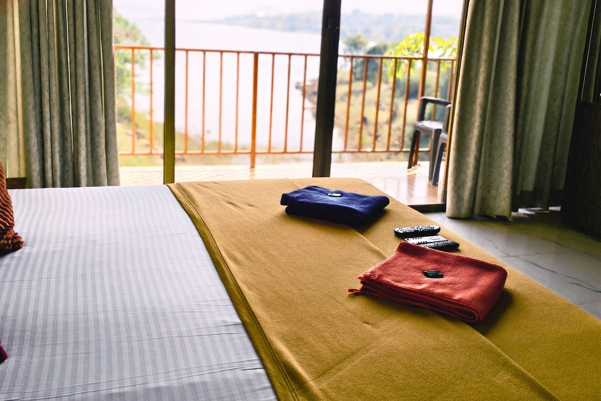Habitación de hotel con una cama, una manta amarilla y vistas al exterior a través de amplias ventanas.
