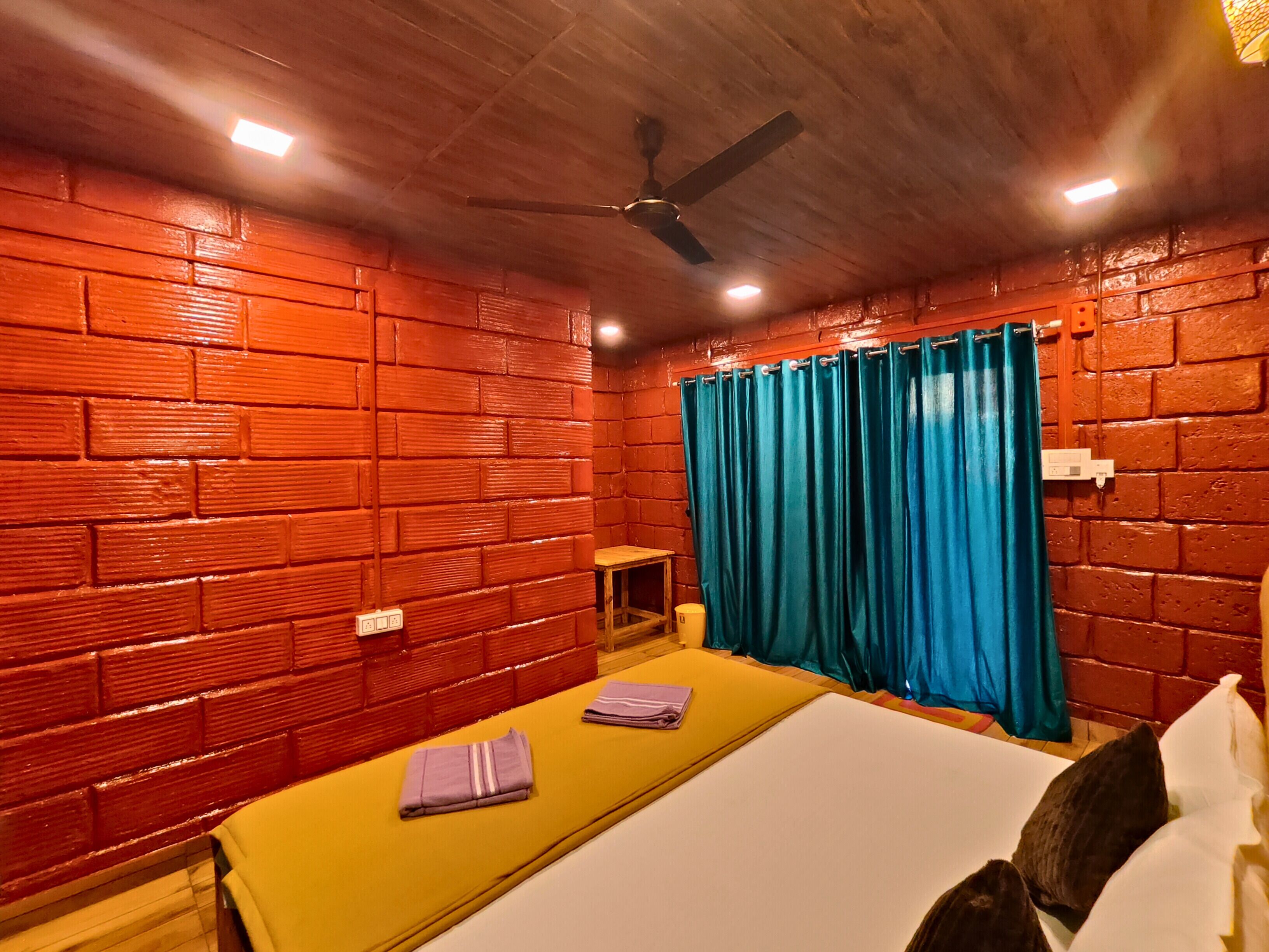 A room with a brick-patterned wall, a bed with a yellow mattress, a blue curtain, and a ceiling fan.