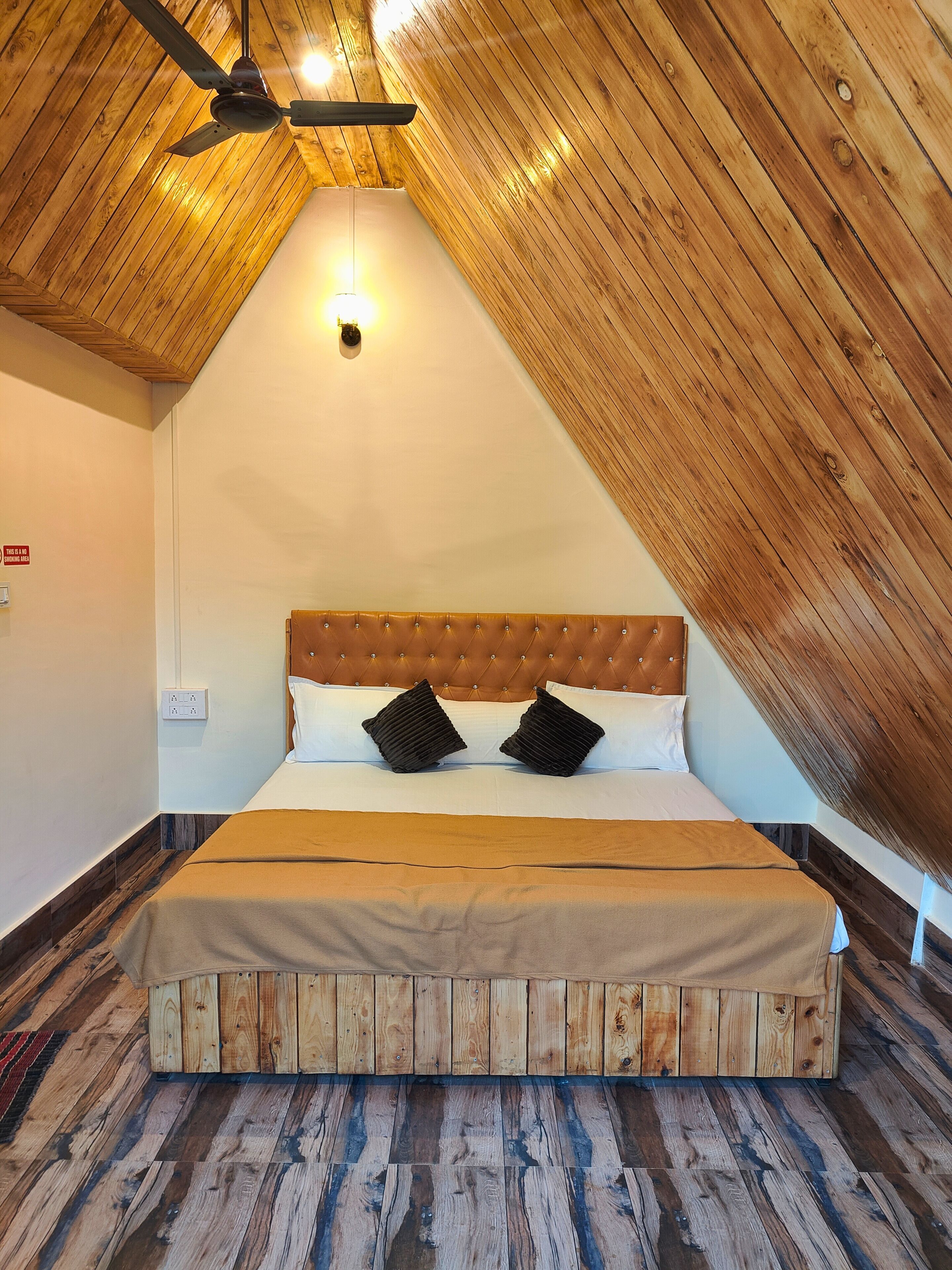 Una habitación con techo inclinado, una cama con cabecera capitonada, dos almohadas negras y un ventilador de techo.