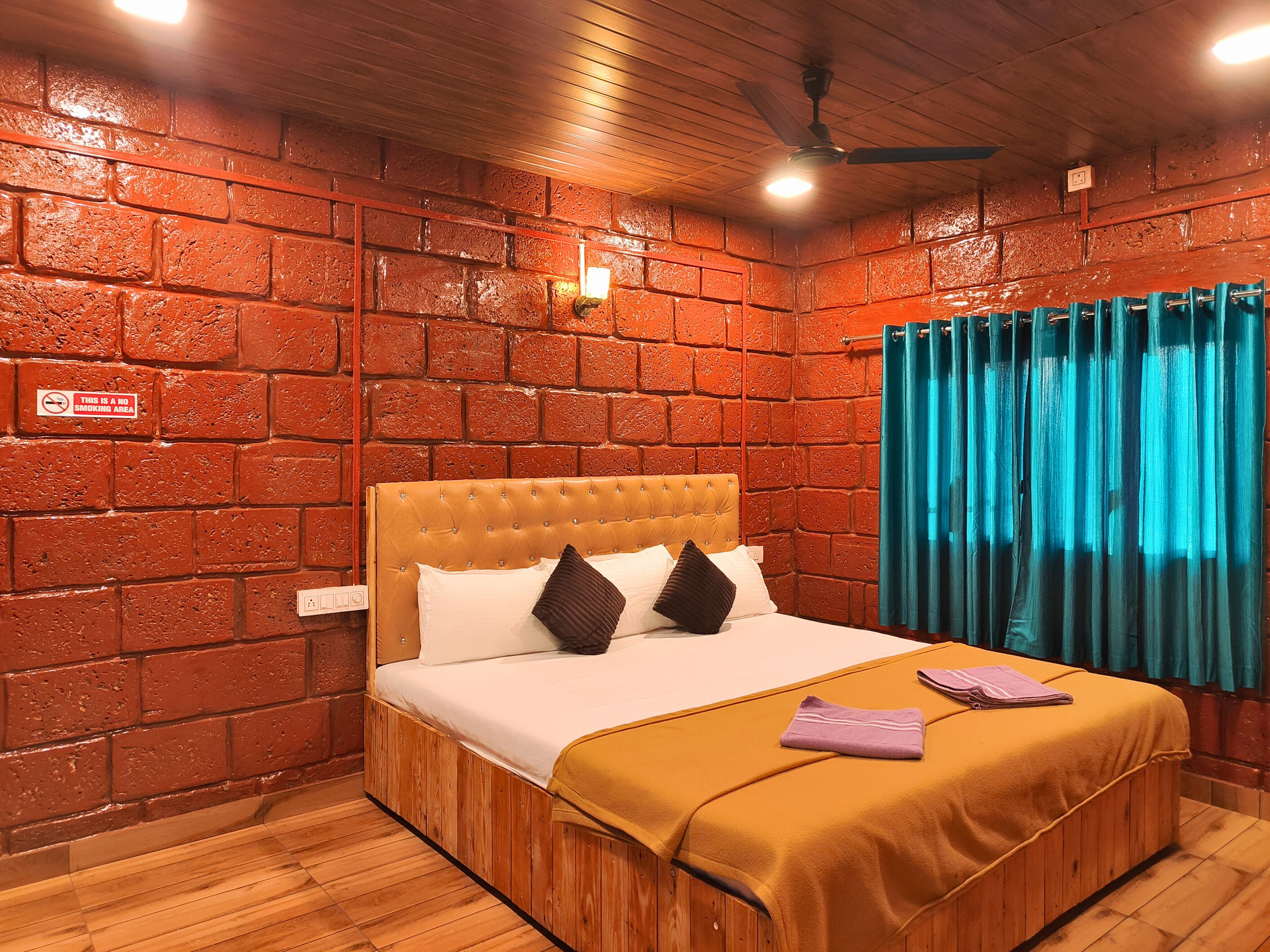 A room with a brick wall, a bed with a headboard, a nightstand, a blue curtain, and a ceiling fan.