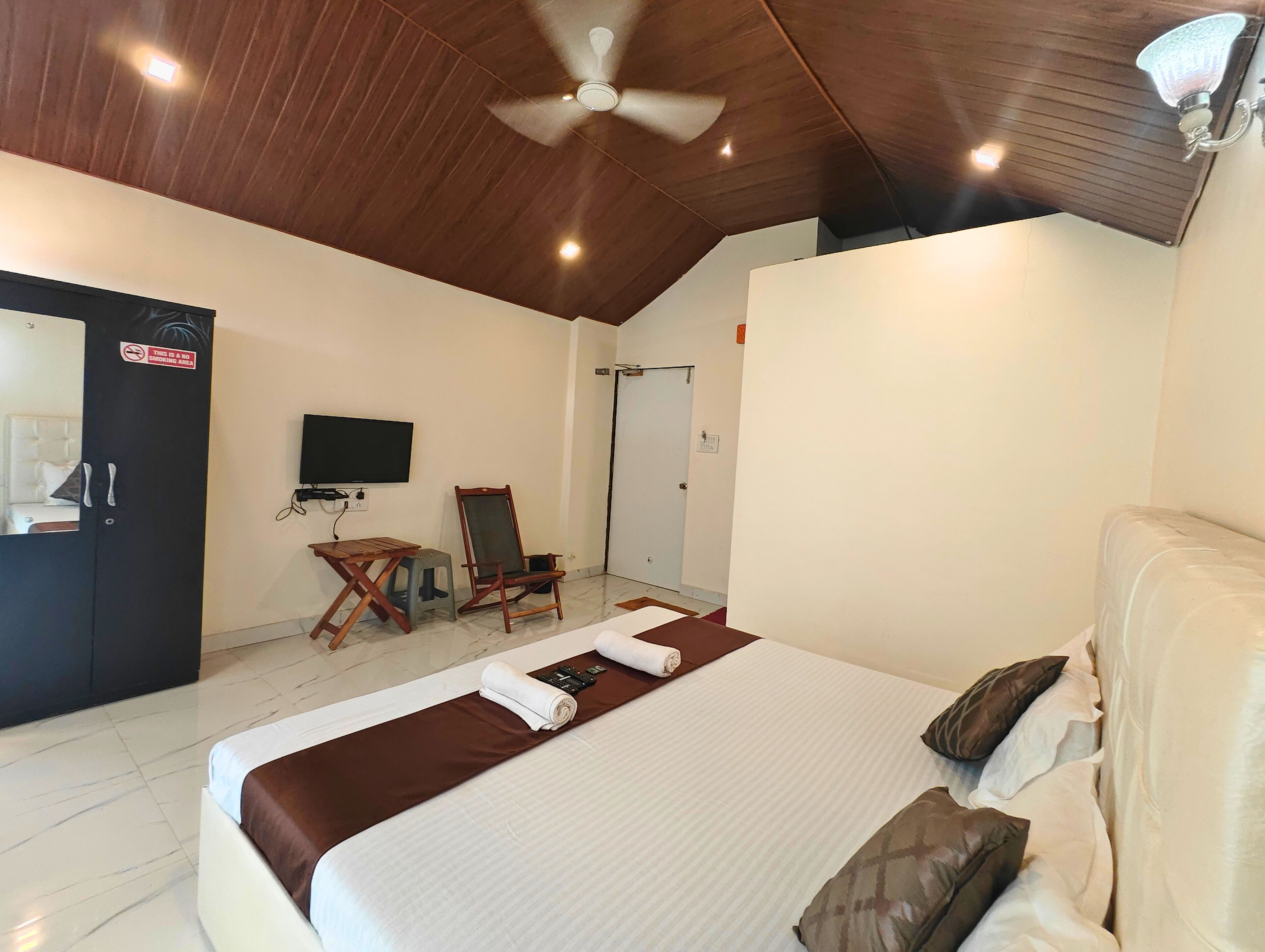 Una habitación de hotel con cama, escritorio, silla, televisor y ventilador de techo.