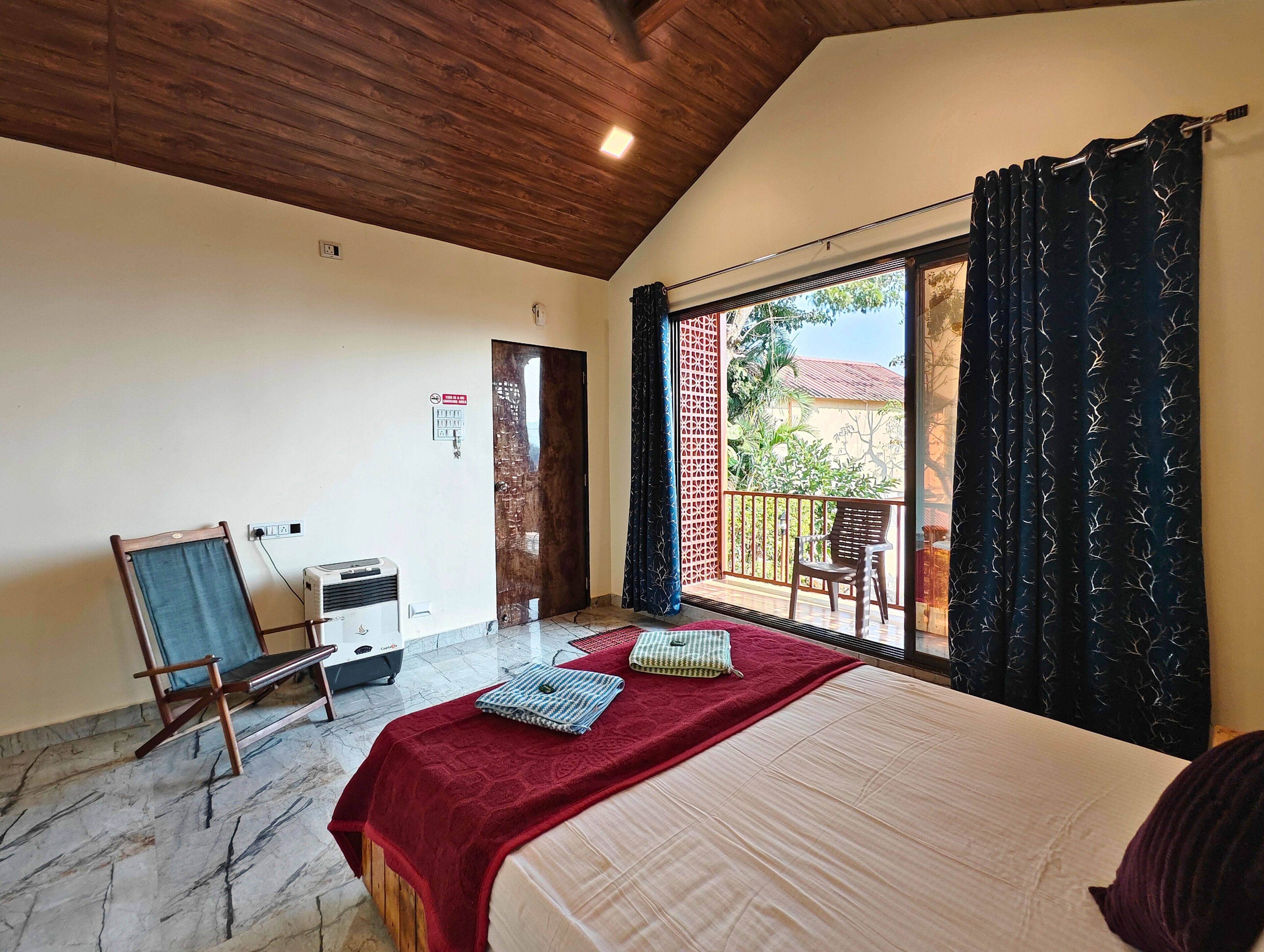 Un dormitorio con cama, escritorio, silla, ventana con cortinas y balcón.