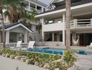 A multi-story building with a swimming pool, outdoor seating, and palm trees. - Romantic Waterfront Villa for 6 (Willemstad)