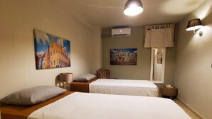 A hotel room with two beds, a nightstand, a lamp, an air conditioning unit, and two paintings on the wall. - Romantic Waterfront Villa for 6 (Willemstad)