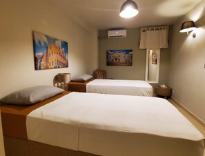 A hotel room with two beds, a nightstand, a lamp, an air conditioning unit, and two paintings on the wall. - Romantic Waterfront Villa for 6 (Willemstad)