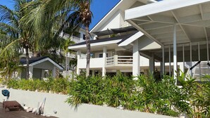 A modern beachfront property with a covered patio, palm trees, and a white building with balconies. - Romantic Waterfront Villa for 6 (Willemstad)