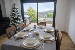 Une table à manger dressée pour six personnes, avec assiettes, verres et couverts, un sapin de Noël, et une vue sur un balcon aménagé avec du mobilier d’extérieur.