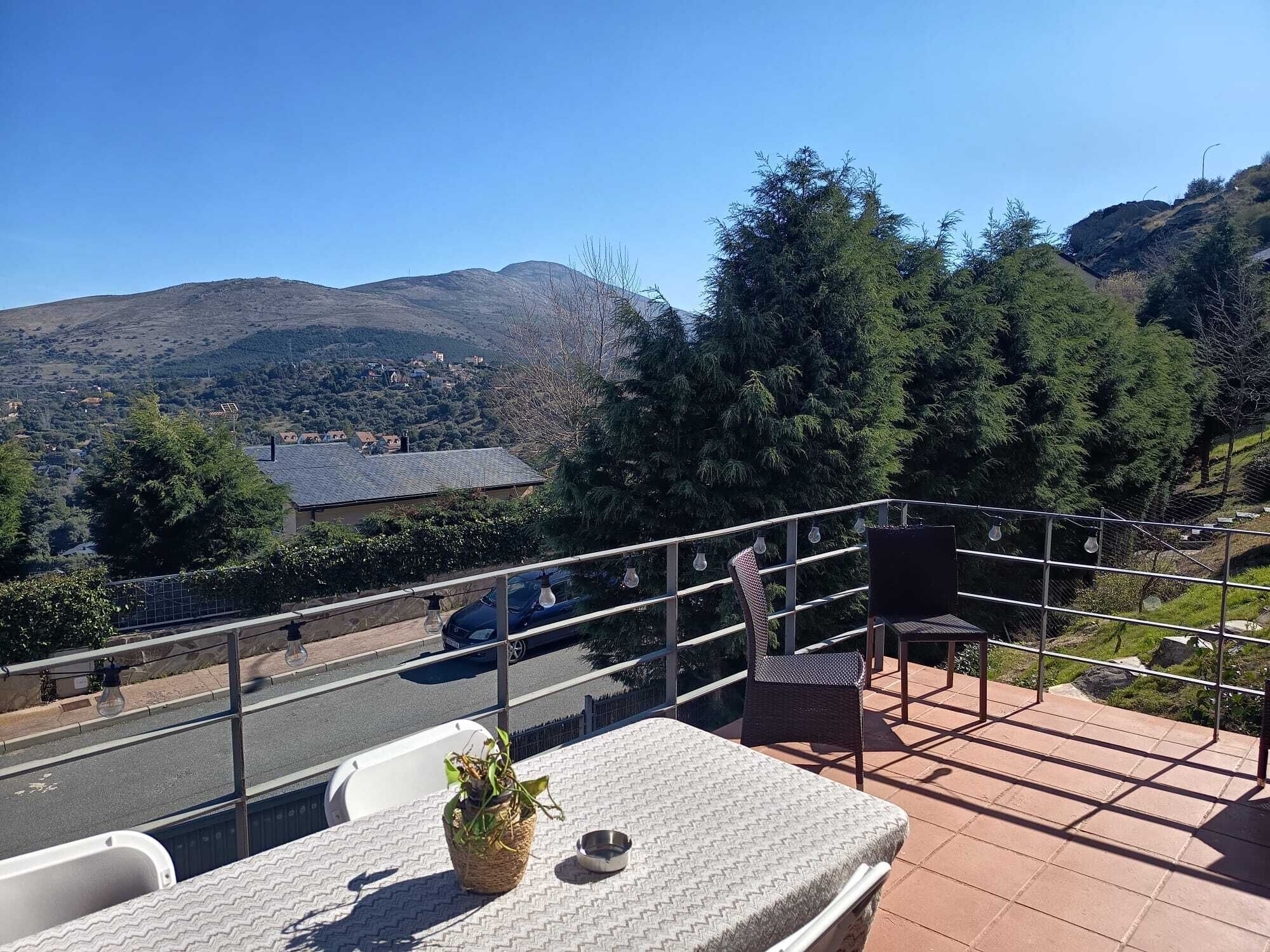 A balcony with a view of a mountainous landscape, a chair, a table, and a potted plant.