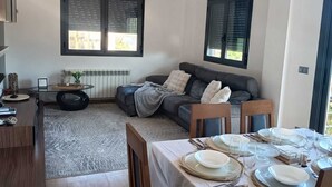 Moderni olohuone, jossa on ruokailutila, sohva ja suuret ikkunat.