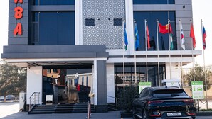 Un edificio con fachada moderna, varias banderas y un SUV negro estacionado en la entrada.