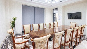 Un salón de conferencias con una gran mesa ovalada, sillas a juego, una planta en maceta y un moderno candelabro.