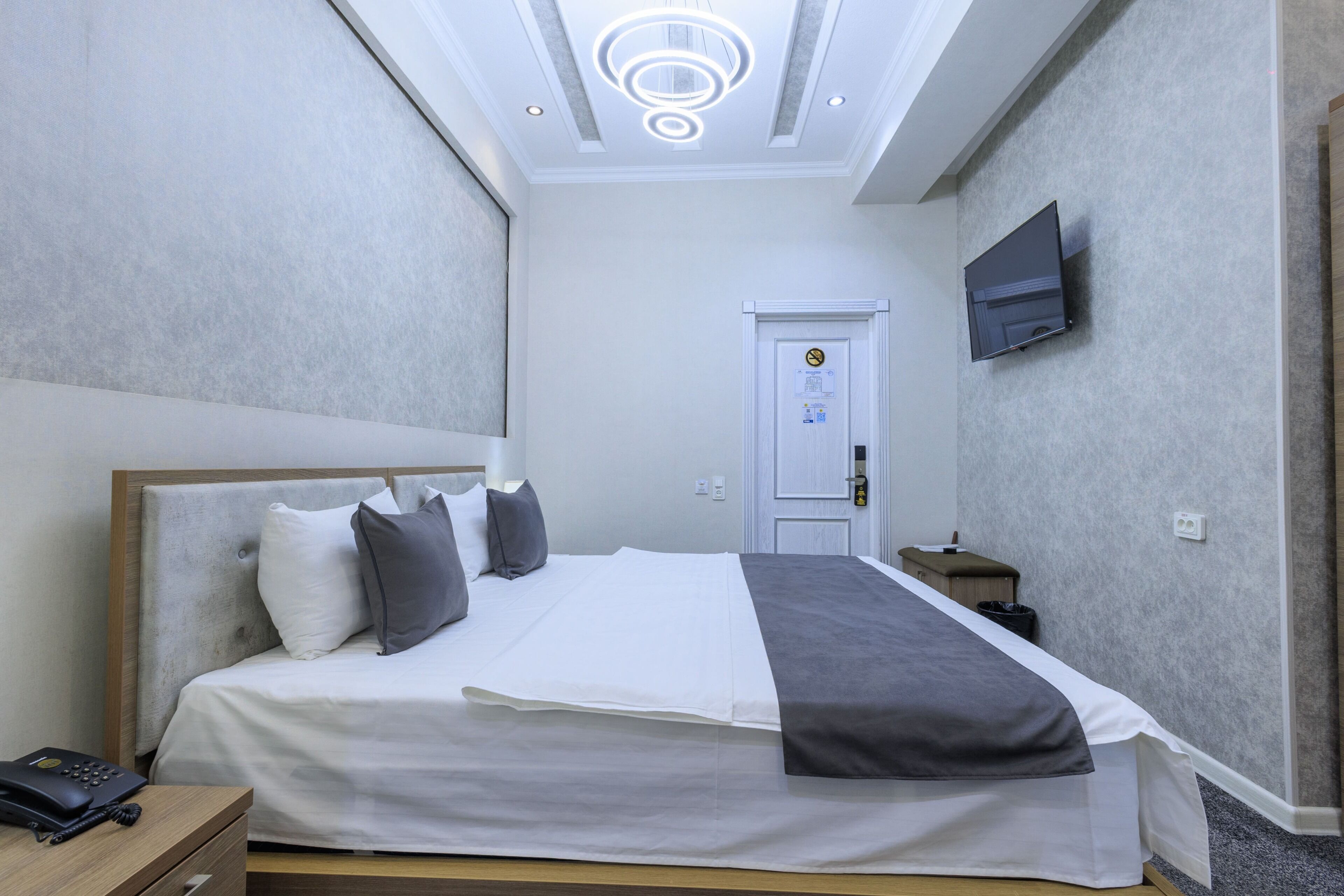 Una habitación de hotel con cama, mesita de noche, lámpara y televisor montado en la pared.