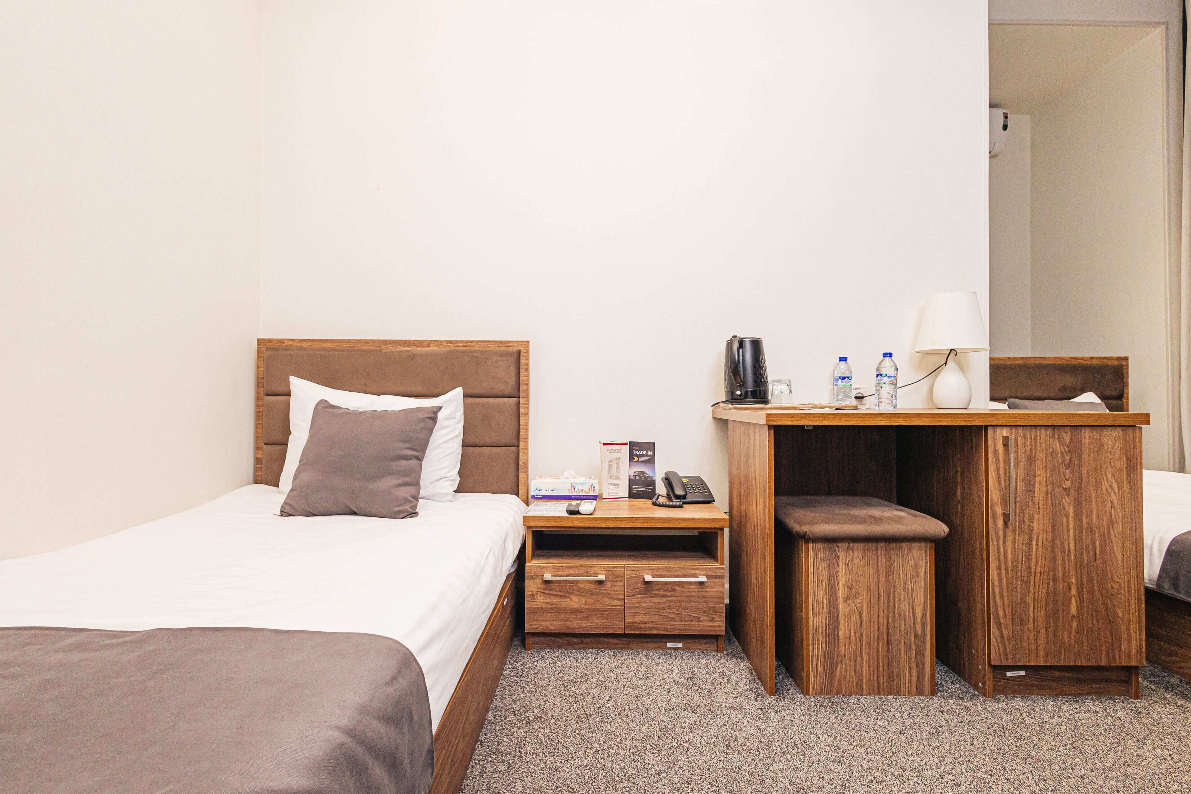A hotel room with a bed, a desk, a chair, a telephone, and a lamp.