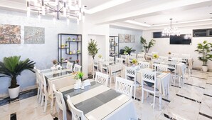 Un comedor moderno con mobiliario blanco, varias mesas y plantas decorativas.