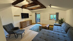 Un salon comprenant un canapé, un fauteuil, un téléviseur, un meuble en bois et une fenêtre.