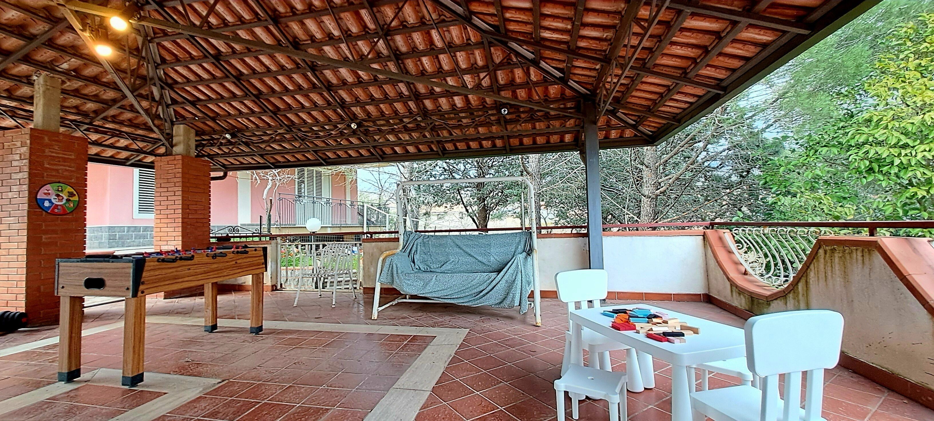 An outdoor patio with a foosball table, a table with toys, and a covered seating area.