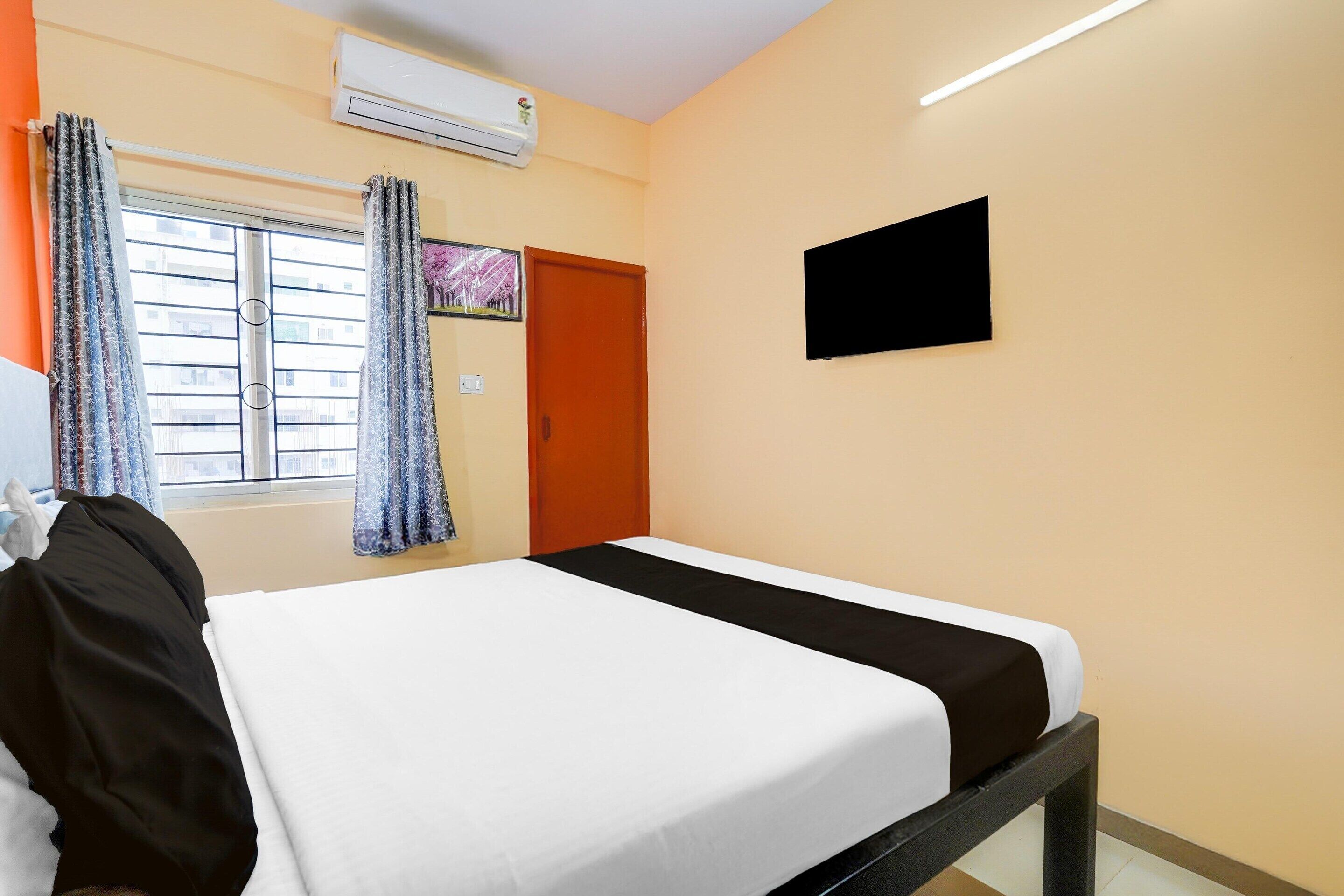 A room with a bed, an air conditioner, a television, and a window with curtains.