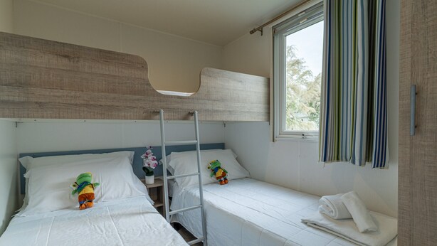 A room with bunk beds, a ladder, a window with curtains, and a small table with a flower vase. - Vigna Sul Mar Family Collection (Comacchio)
