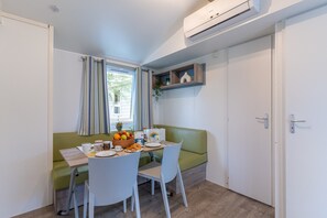 A compact room with a dining table, chairs, a green sofa, and a small shelf with decorative items. - Vigna Sul Mar Family Collection (Comacchio)