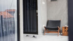 A room with a sliding glass door, a black chair, a small wooden side table, and a pair of shoes on the floor. - Escotel Krisnantara Canggu (Tibubeneng)