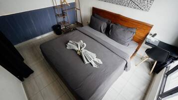 Una cama bien hecha con una toalla y flores, un cabecero de madera, un estante metálico y una silla negra.