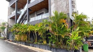 A modern building with a staircase, multiple balconies, and a row of tropical plants along the sidewalk. - Escotel Krisnantara Canggu (Tibubeneng)