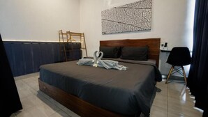 A hotel room with a bed, a wooden headboard, a wall-mounted abstract art piece, a desk with a chair, and a radiator. - Escotel Krisnantara Canggu (Tibubeneng)