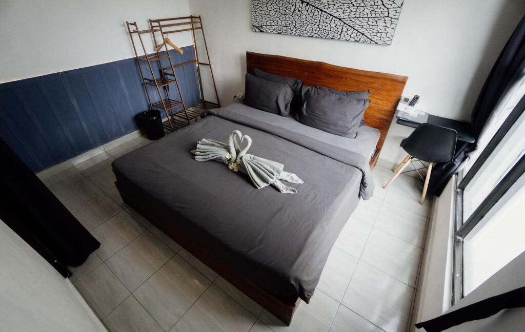 Habitación de hotel con cama, cabecera de madera, una obra de arte abstracta en la pared, una silla negra y una ventana con cortinas.