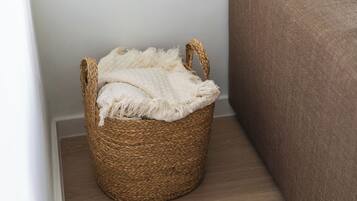 A woven basket with handles, placed on a wooden floor next to a brown upholstered piece of furniture.