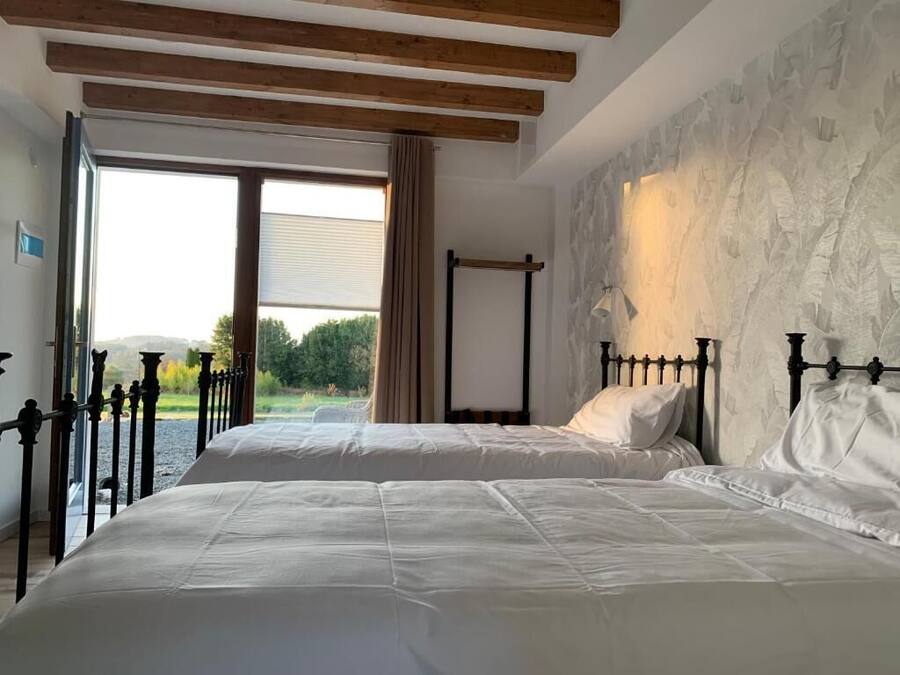 Ein Schlafzimmer mit zwei Betten, einer Steinwand, einem Fenster mit Vorhängen und einem Holzbalken an der Decke.