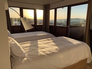 A bedroom with a bed, a desk lamp, and large windows with a view of a landscape. - Hotel Rural Rectoral de Boente (Arzua)