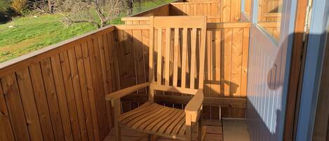 Terraza de madera con una silla de madera y un ventanal de vidrio que da a un espacio cubierto.
