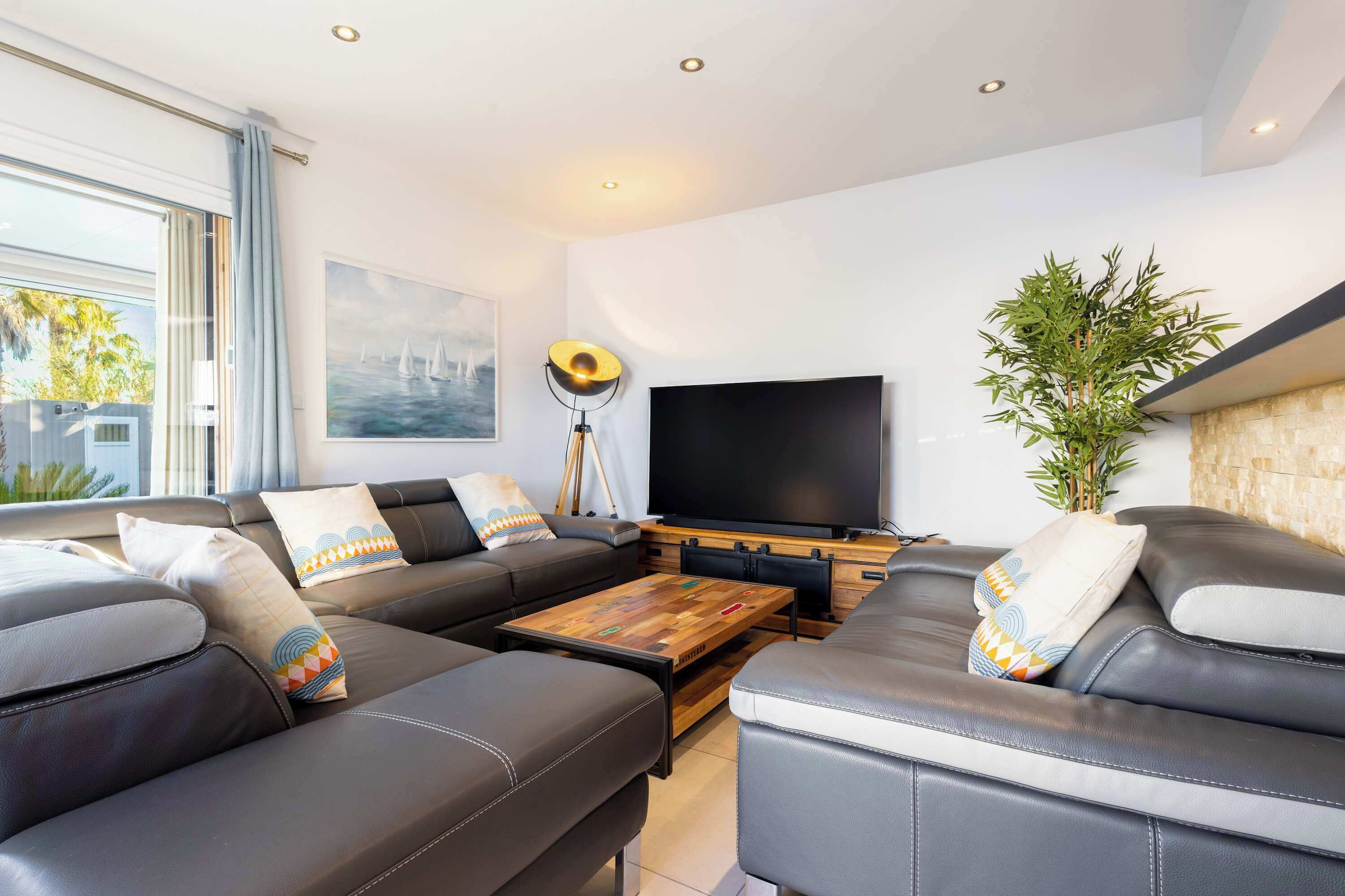 A modern living room with a sofa set, a flat-screen TV, a coffee table, and a large window with curtains.