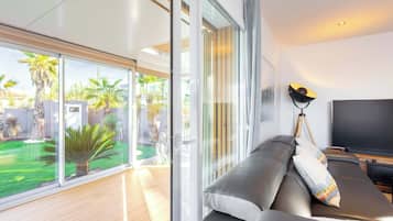 A modern living room with a sofa, a TV, and a large sliding glass door leading to a garden.
