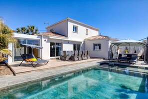 Ein modernes Haus mit Swimmingpool, Sitzgelegenheit im Freien und einer überdachten Terrasse.