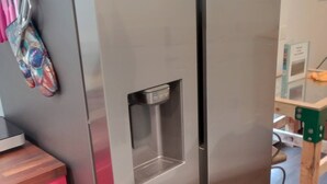 A stainless steel refrigerator with a water dispenser, a wooden cabinet, and a red drawer unit. - Cozy Container: A Shipping Container Retreat for Pups & People. (Soldotna)