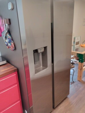 A stainless steel refrigerator with a water dispenser, a wooden cabinet, and a red drawer unit.