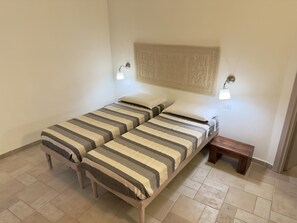 Een tweepersoonsbed met gestreept beddengoed, twee bedlampjes, een klein houten nachtkastje en een decoratieve wanddecoratie.
