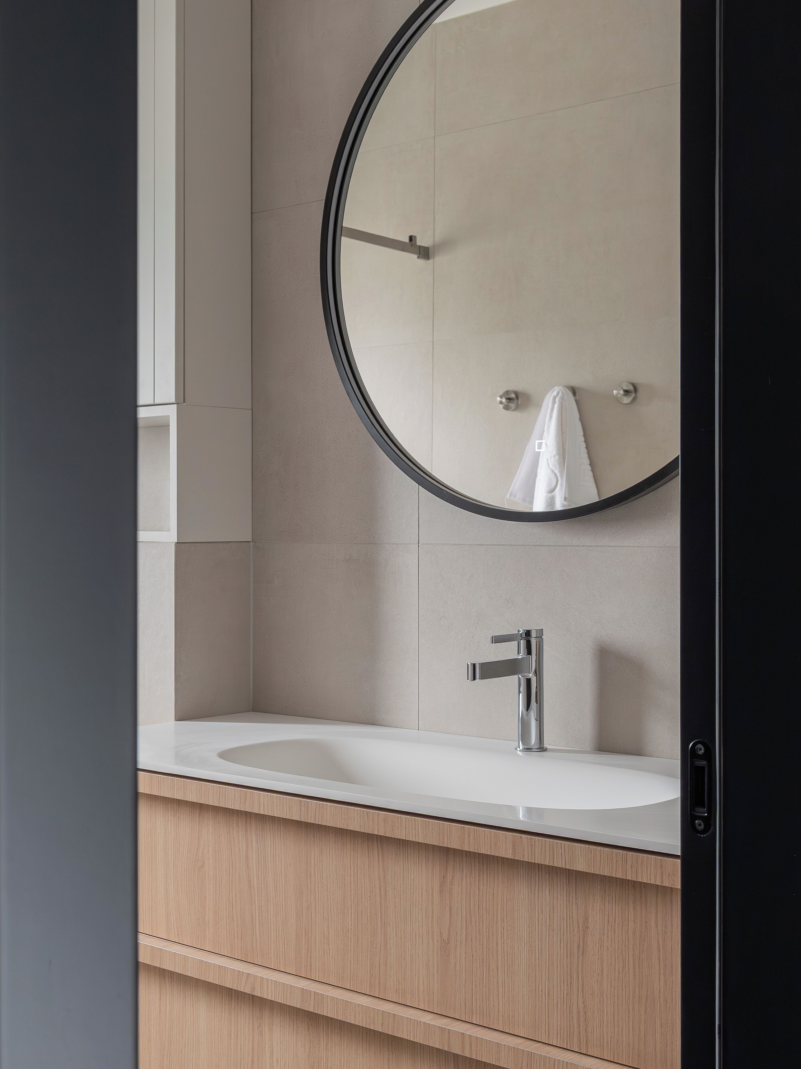 Une salle de bain avec un miroir rond, un lavabo blanc et un meuble-lavabo en bois.