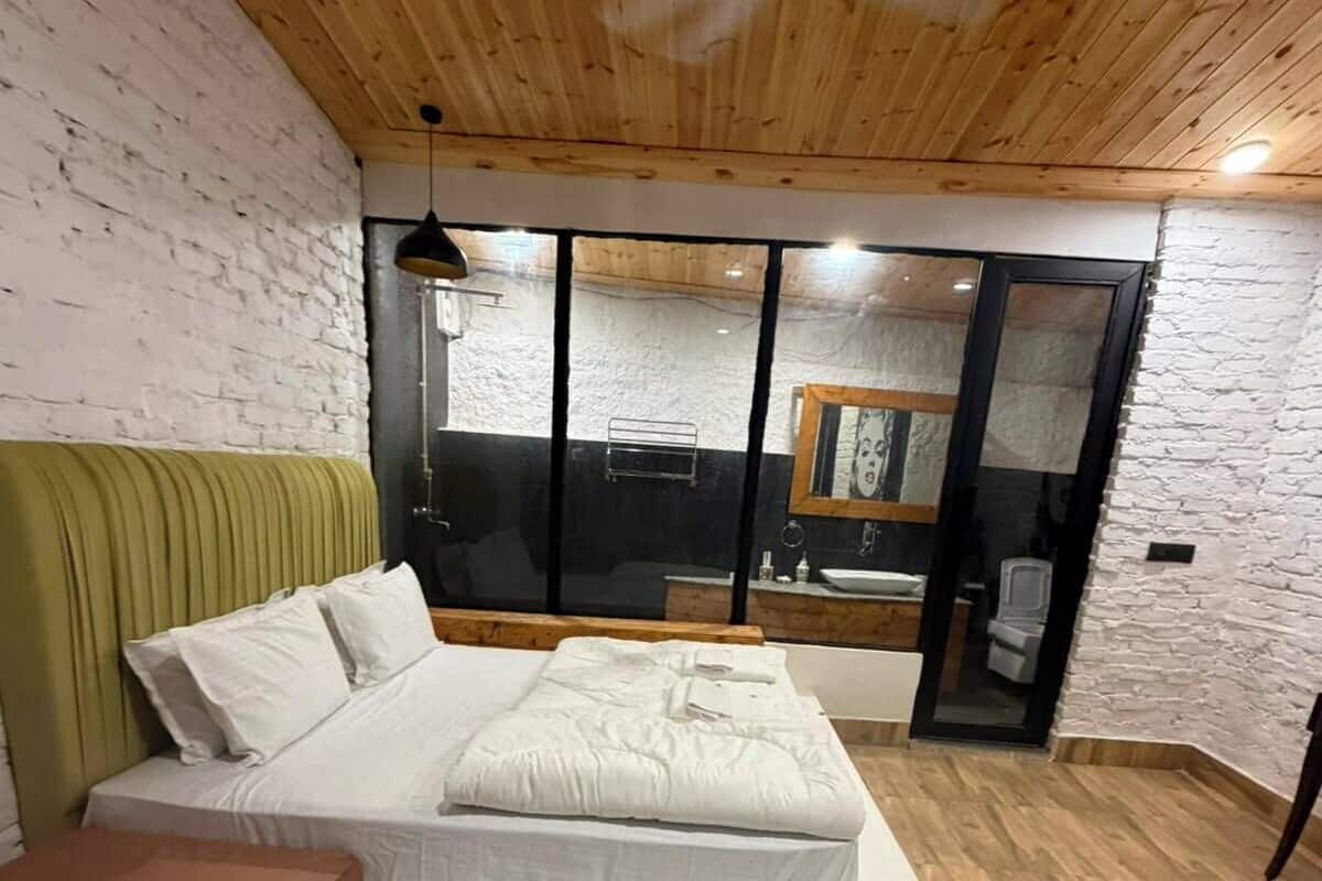 Een slaapkamer met een houten plafond, een bed met wit beddengoed, een bekleden hoofdeinde in groen en een houten vloer.