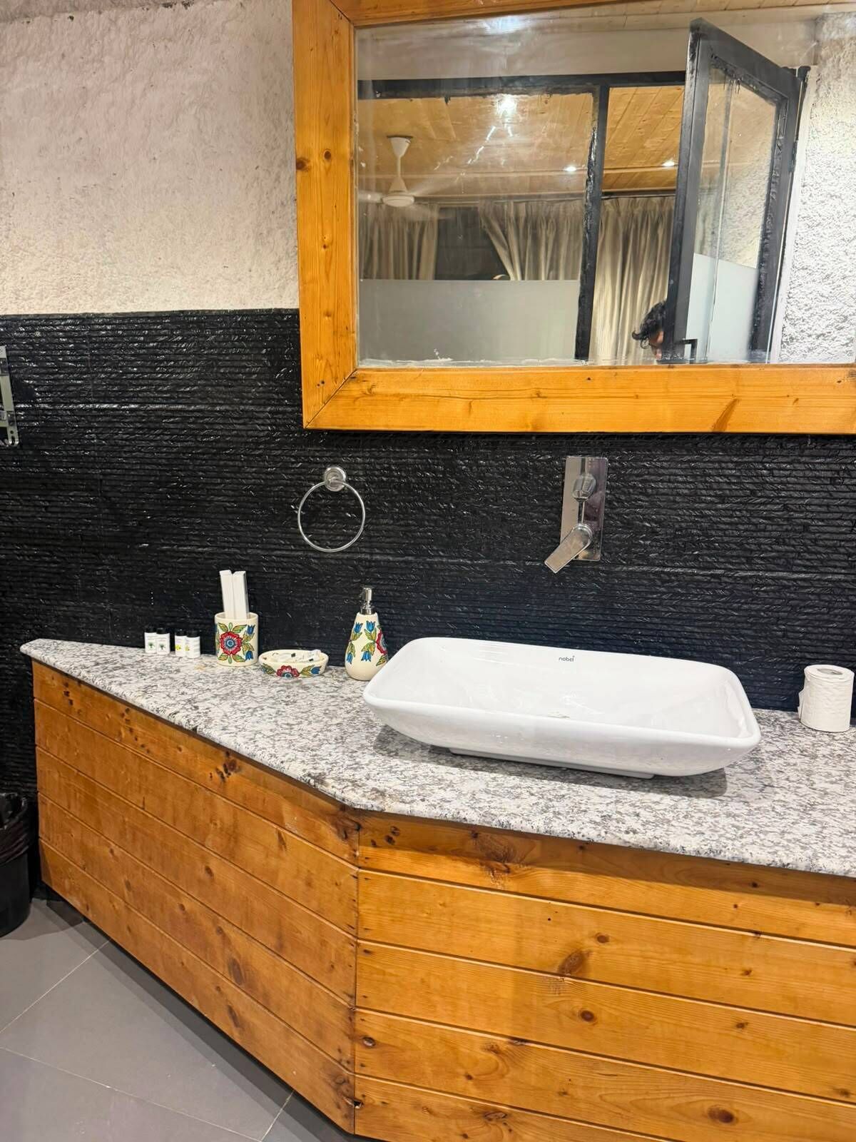 A bathroom with a wooden vanity, a white sink, a mirror, and a black and white tiled backsplash.