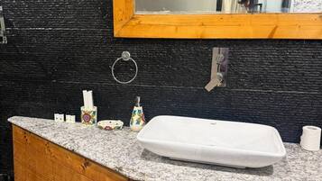 A bathroom with a wooden vanity, a white sink, a mirror, and a black and white tiled backsplash.