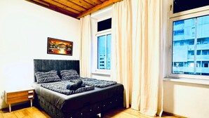 A bedroom with a bed, wooden flooring, a ceiling light, a window with curtains, and a painting on the wall. - Spacious Private Room Near FAC Platz (Wien)