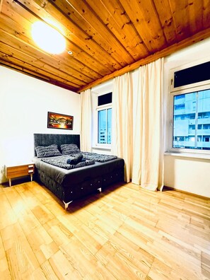 A bedroom with a bed, wooden flooring, a ceiling light, a window with curtains, and a painting on the wall. - Spacious Private Room Near FAC Platz (Wien)
