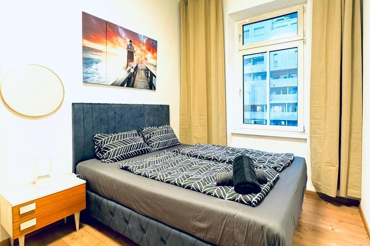 A bedroom with a bed, a nightstand, a window with curtains, and a painting on the wall.
