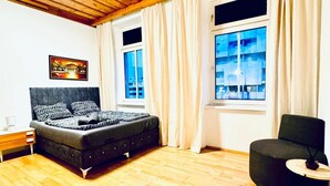 A room with a bed, a chair, a wooden floor, and a window with curtains. - Spacious Private Room Near FAC Platz (Wien)