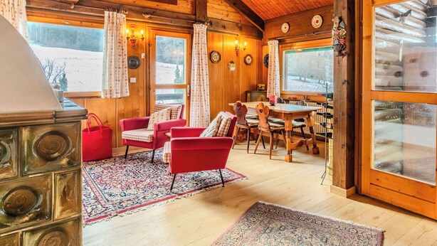 Ein gemütliches Blockhaus-Interieur mit Holzwänden, einer Essecke und einem großen Fenster mit Blick auf die verschneite Landschaft.