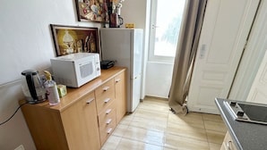 Une cuisine compacte équipée d’un four à micro-ondes, d’un petit placard, d’un lave-linge et d’une fenêtre avec des rideaux.